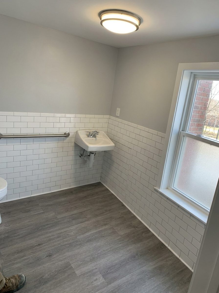 After - the same commercial restroom with new tile, vanity, grab bar, and flooring