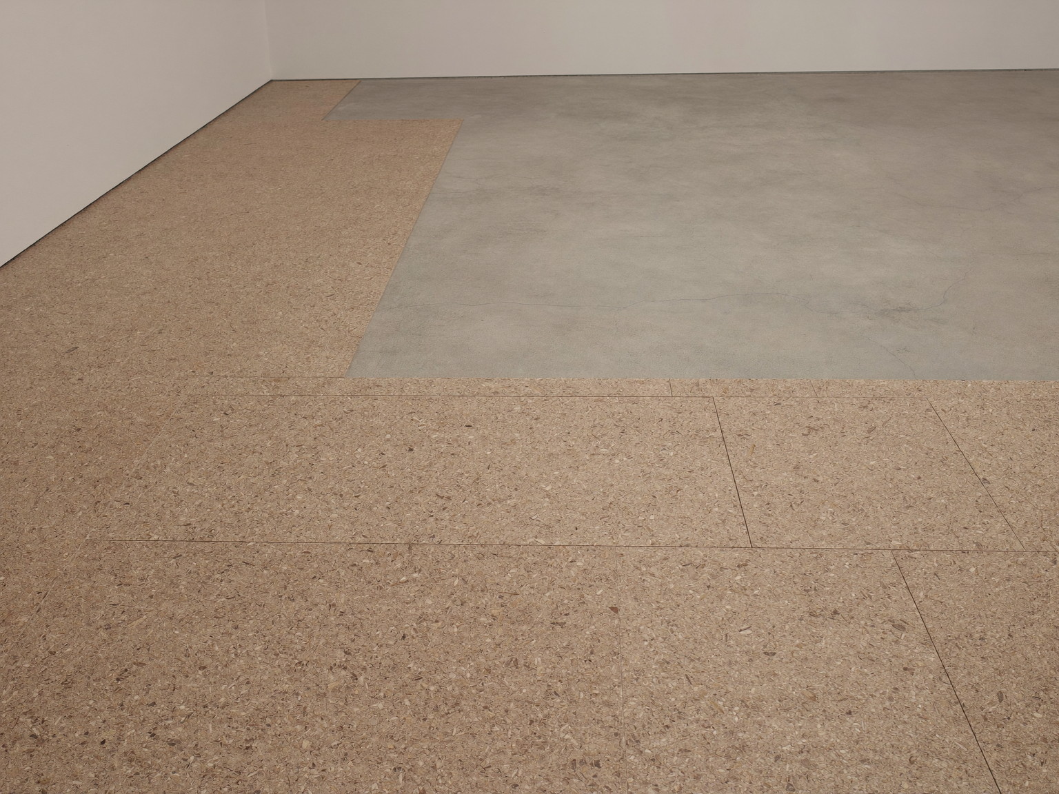 Cork floor tiles mid-installation across a clean rowhouse basement floor, smooth bare concrete still showing beside the finished cork, the room completely empty, soft work light
