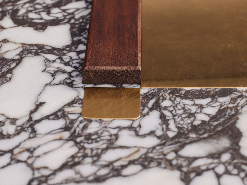 Detail study of richly veined marble beside a strip of dark walnut and a small square of unlacquered brass, three rowhouse materials meeting on a flat surface, shallow depth of field