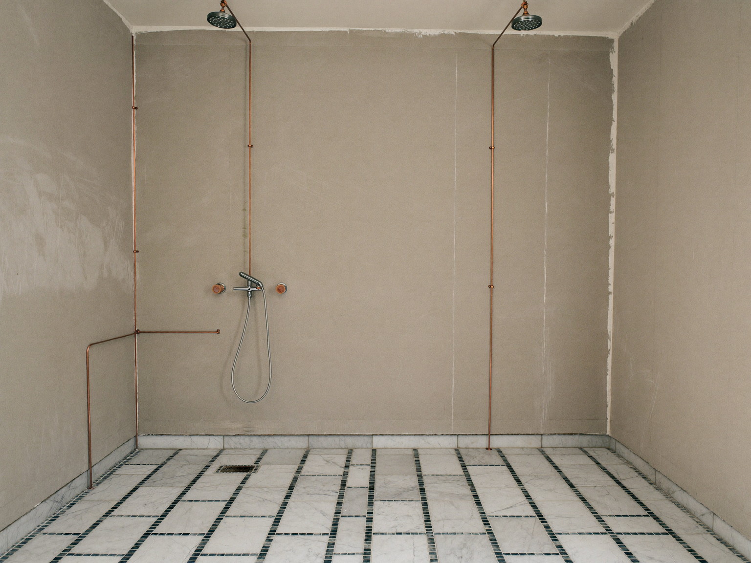 Mid-renovation rowhouse bathroom, tidy and completely empty with no one in it: fresh cement backer board on the walls, new copper supply lines stubbed out, level marble mosaic floor sheets laid dry, clean swept subfloor, soft work light