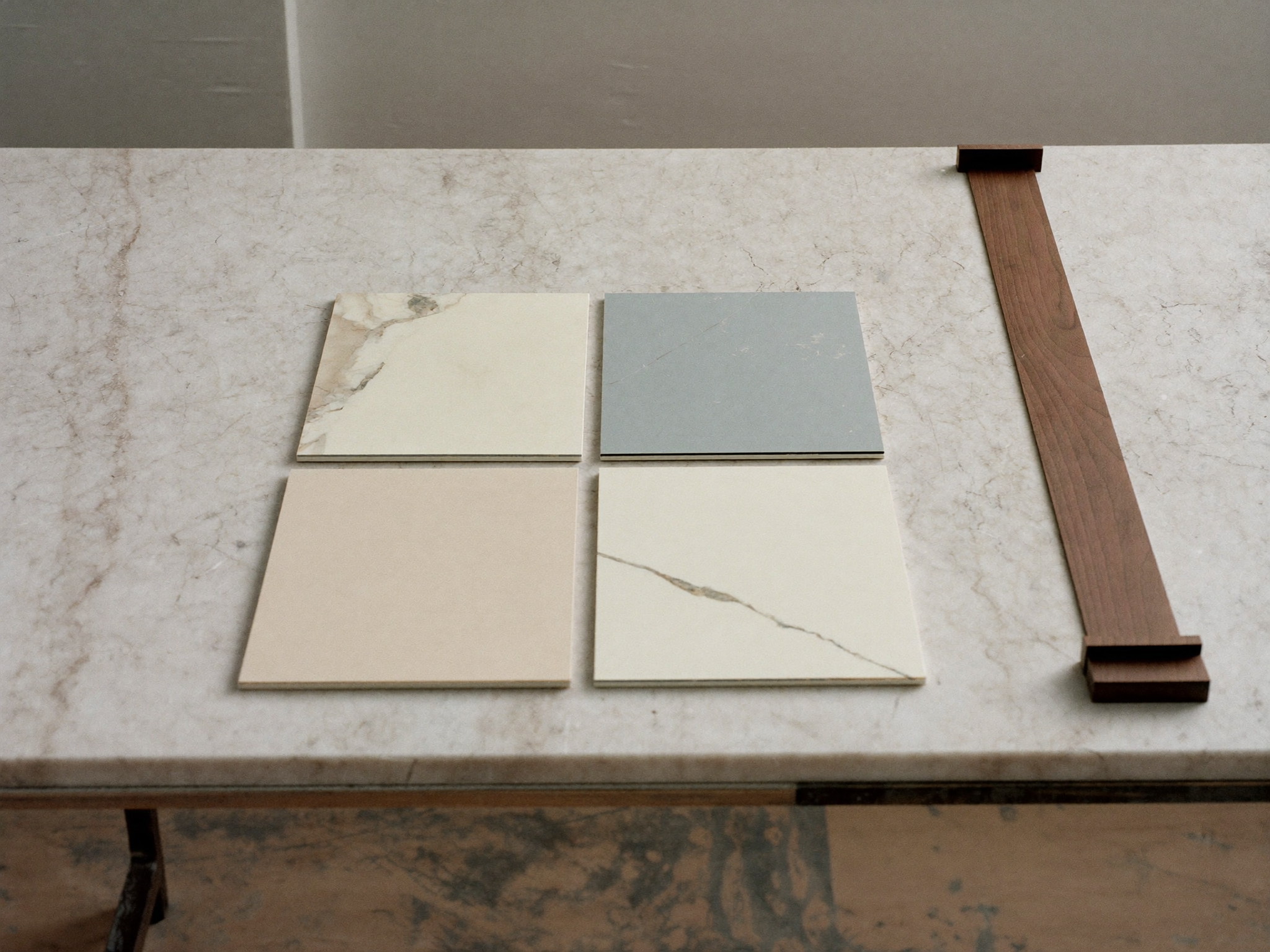 Flat marble slab offcut, painted sample boards in ivory cream and soft gray-blue, and one length of dark walnut trim arranged neatly on a work table in soft window light, plain unmarked materials