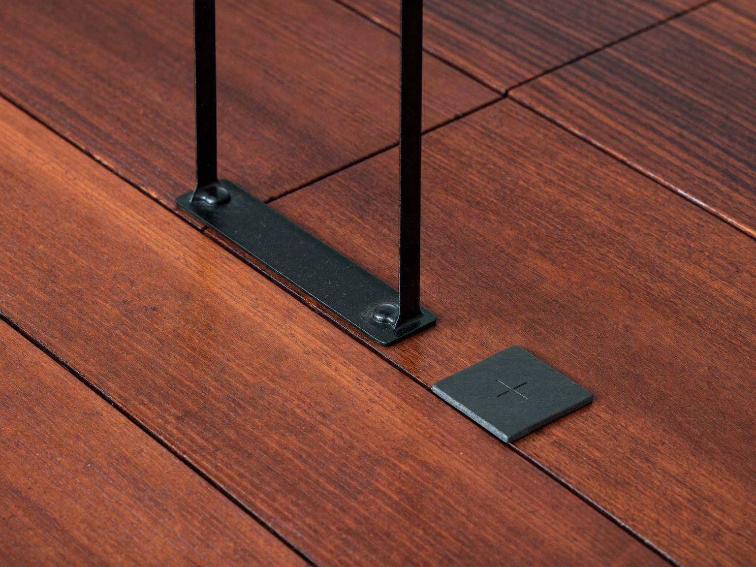 Macro photograph of oiled mahogany deck boards beside a black iron baluster and a small square of slate, three materials meeting cleanly, rich grain detail, shallow depth of field