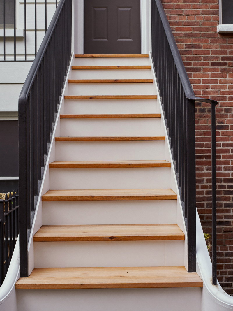 A rebuilt exterior wooden stair behind a Boston rowhouse: mahogany treads, crisp white stringers, simple black iron rail, brick wall alongside, tidy and freshly finished