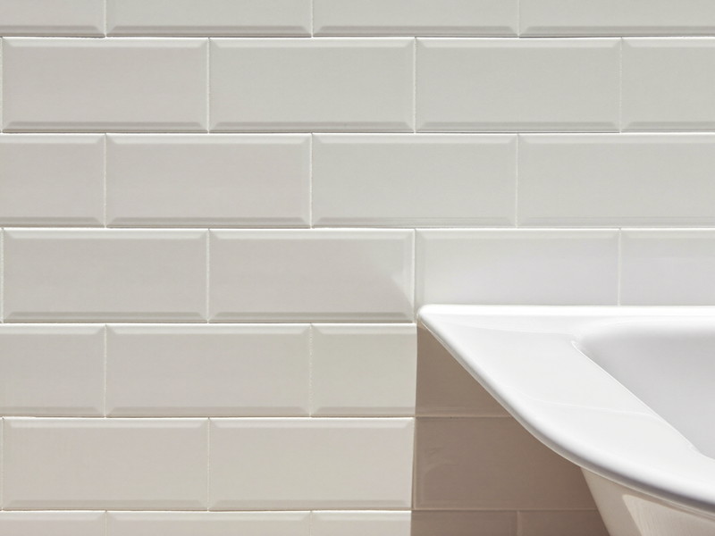 A pristine white basin edge meeting freshly grouted white beveled wall tile in a rowhouse bathroom, crisp bright grout lines, the joint finished with a smooth clean bead, completely bare rim