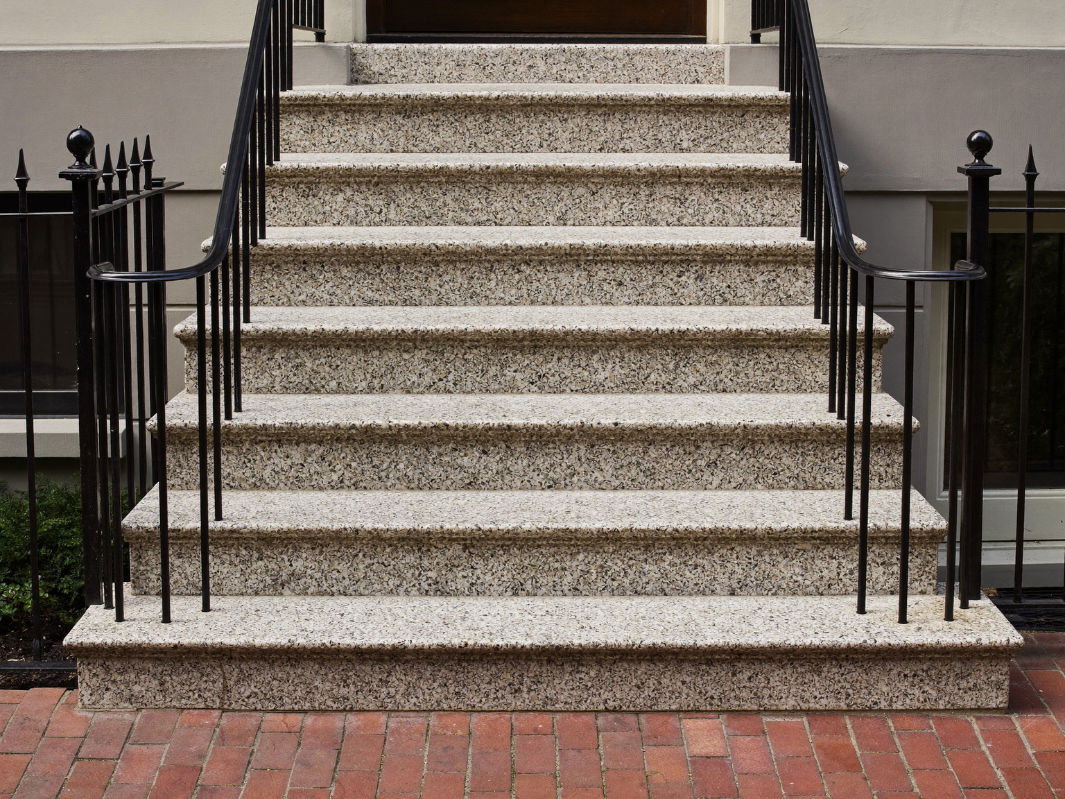 Repaired front entry steps of a Federal-era Boston rowhouse: smooth granite treads over completely plain risers, crisp black iron handrails freshly repainted, brick sidewalk below, tidy and welcoming