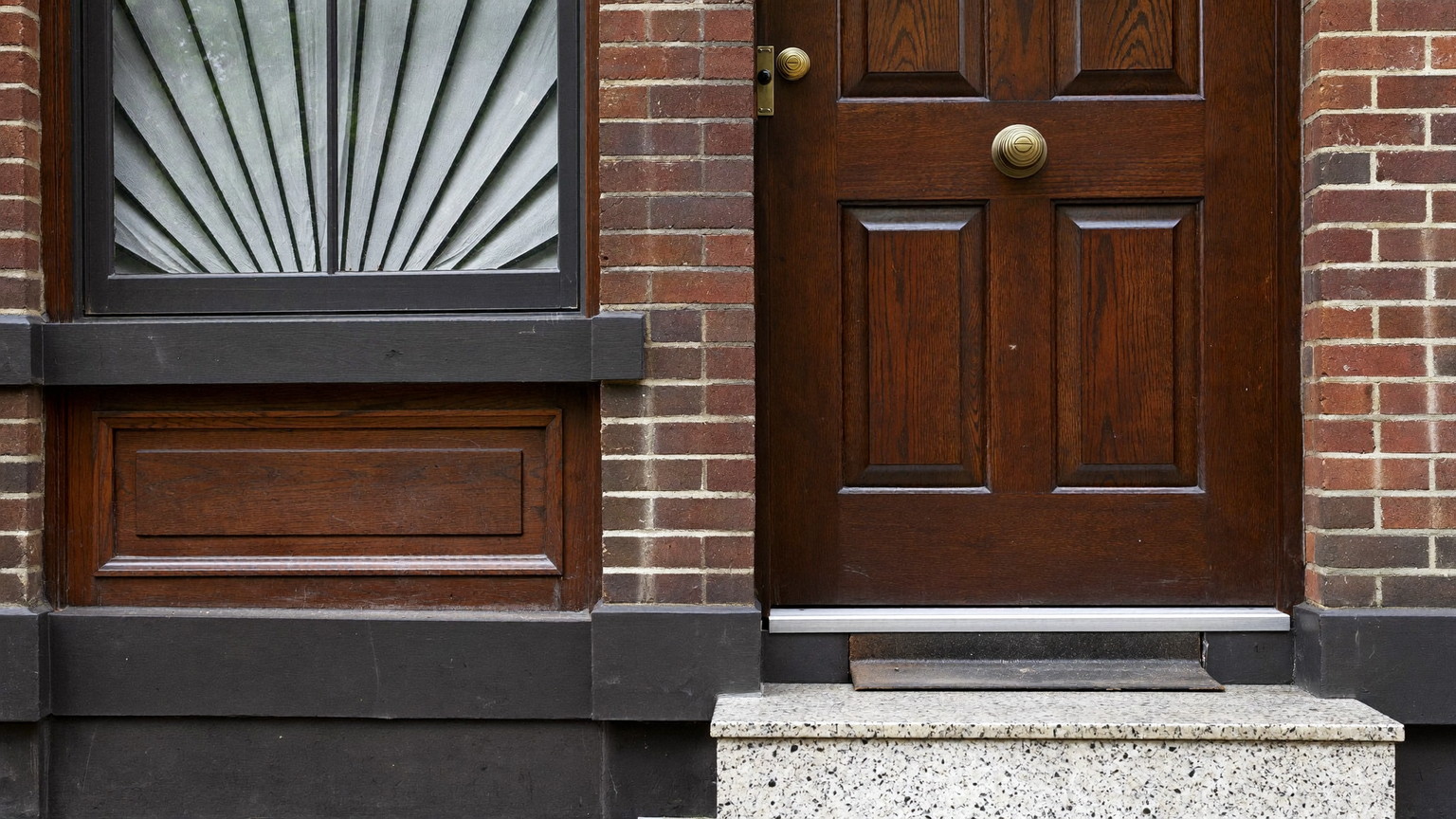 Editorial photograph of a maintained Federal-era rowhouse entry in Beacon Hill Boston: freshly oiled dark wood door under a fanlight window, polished but completely plain brass ball knob, swept granite steps, black iron boot scraper, brick facade