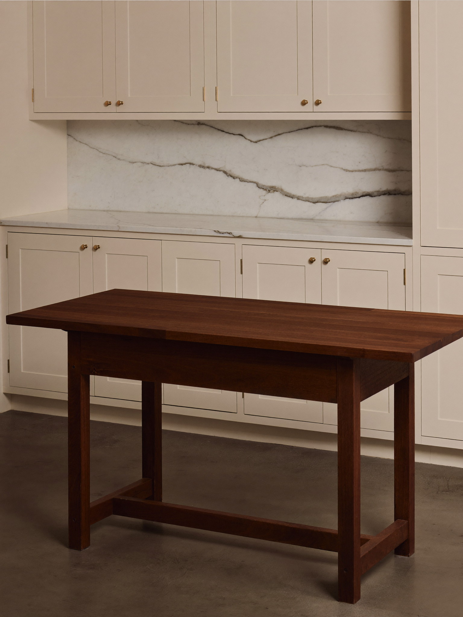 A narrow dark walnut work table serving as an island in a compact Beacon Hill rowhouse kitchen, white marble counters beyond, ivory inset cabinets with brass latches, morning light, every surface freshly wiped and completely clear