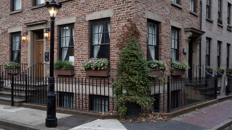 A quiet Beacon Hill Boston corner in soft evening light: brick rowhouse facades, black iron boot scrapers and rails, a gas lantern glowing, window boxes of green ivy, brick sidewalk