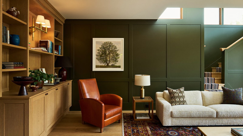 Finished lower-level family room with olive walls, oak shelving, and warm layered lighting