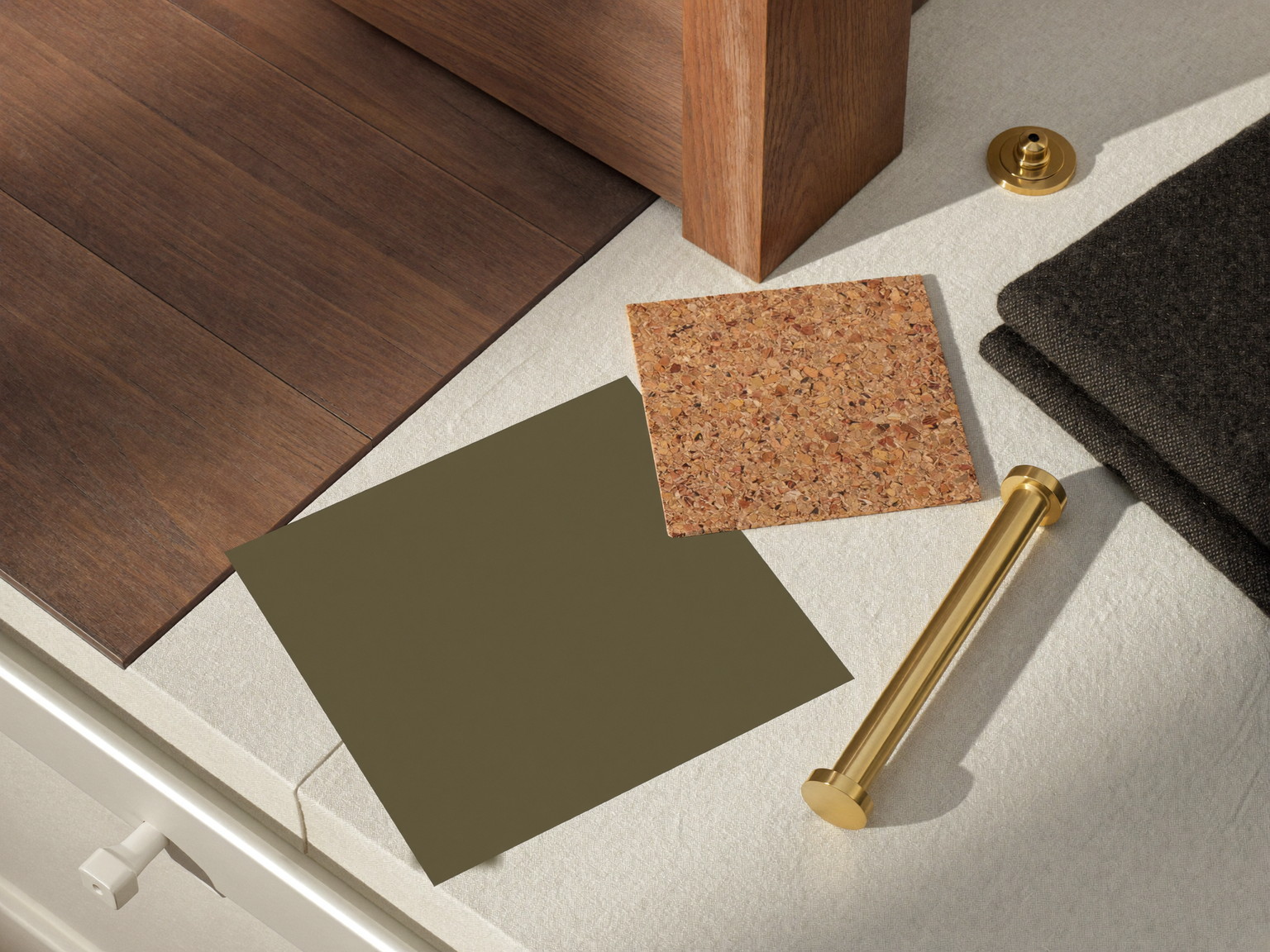 Material still life: oak-look vinyl plank, oak stair tread, olive paint swatch, cork panel, brass hardware, and charcoal wool on cream linen