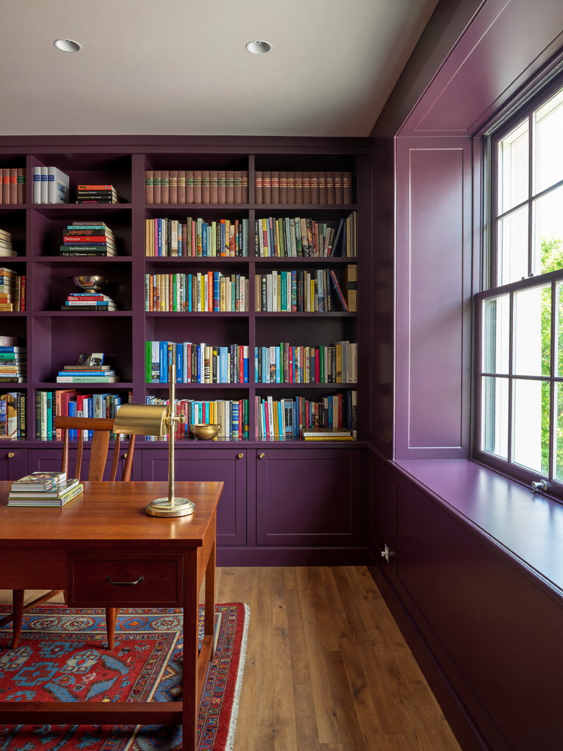 Finished lower-level home library and office with aubergine built-in bookshelves, walnut desk, and brass task lamp
