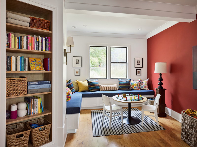 Colorful finished lower-level playroom with navy window-seat bench, game table, and clay-red accent wall