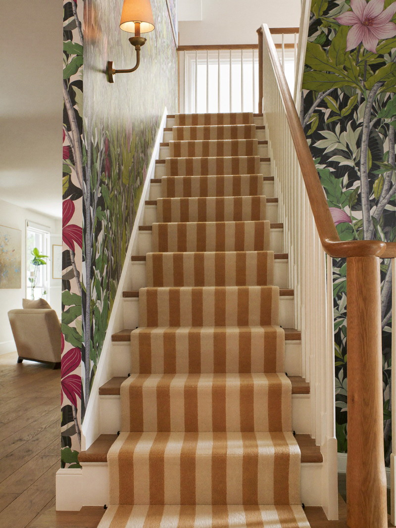 Staircase with striped runner and botanical wallpaper leading down to a finished lower level