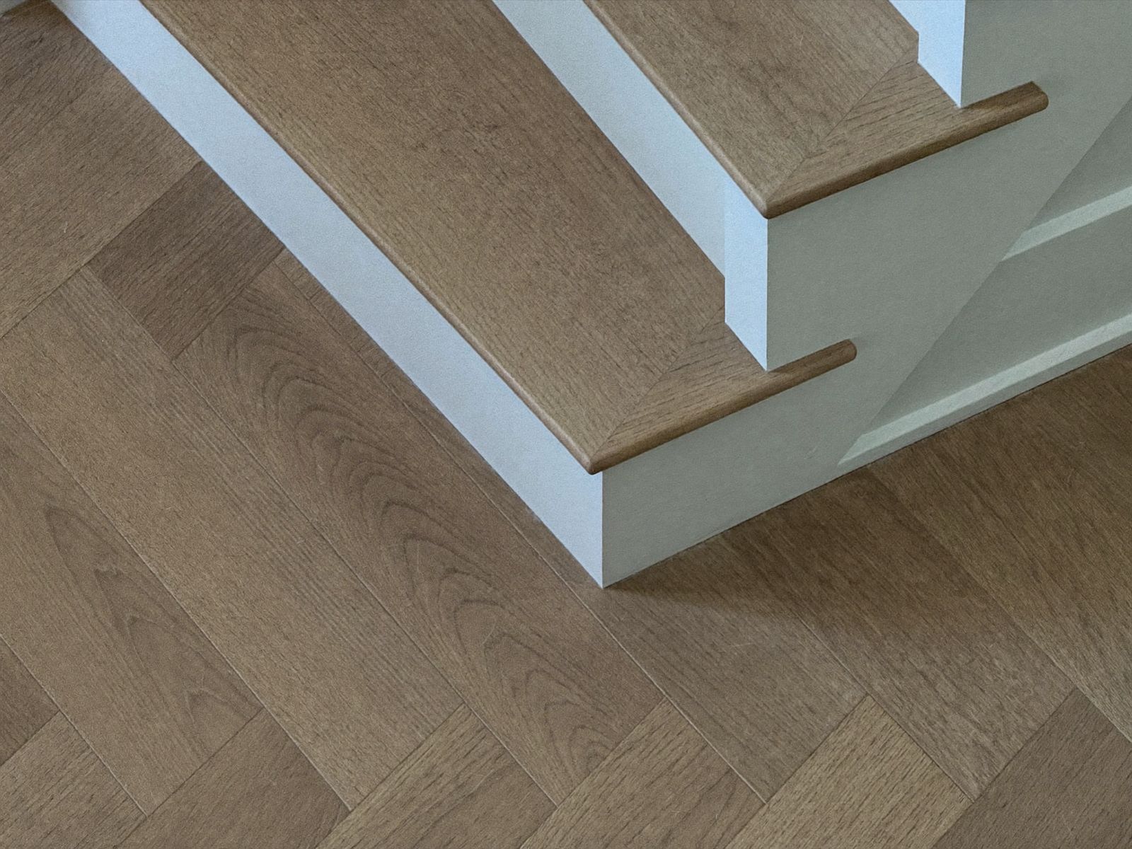 Herringbone vinyl plank flooring meeting oak stair treads in a basement