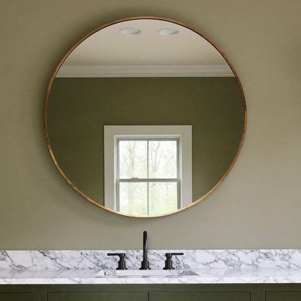 Round brass mirror over a marble vanity top with a matte black faucet