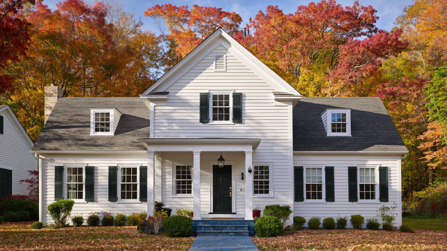 Beautifully maintained white New England Cape with deep green shutters and immaculate trim in autumn light