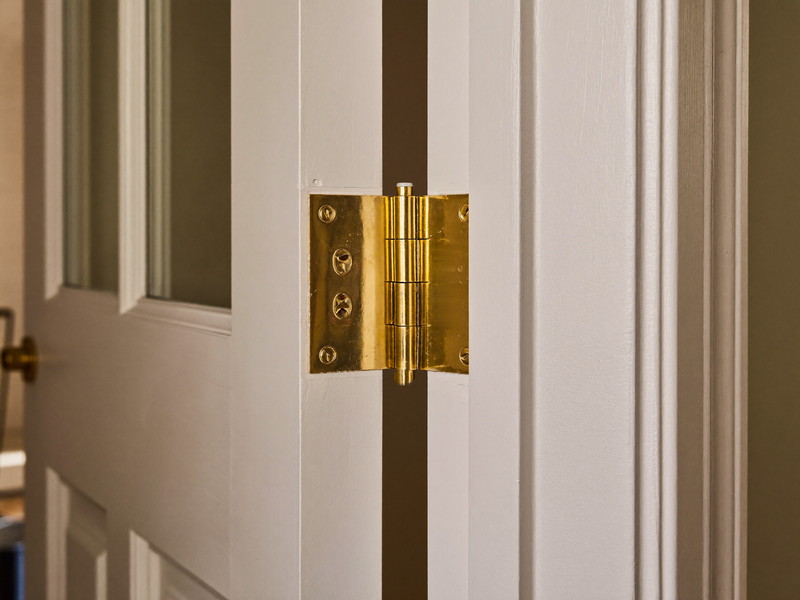 Close detail of a new bronze hinge mortised cleanly into the edge of a white painted door