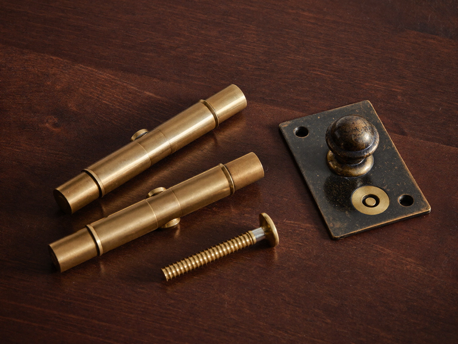 Still life of quality door hardware on dark stained wood: brass hinges, a bronze knob, and matching screws