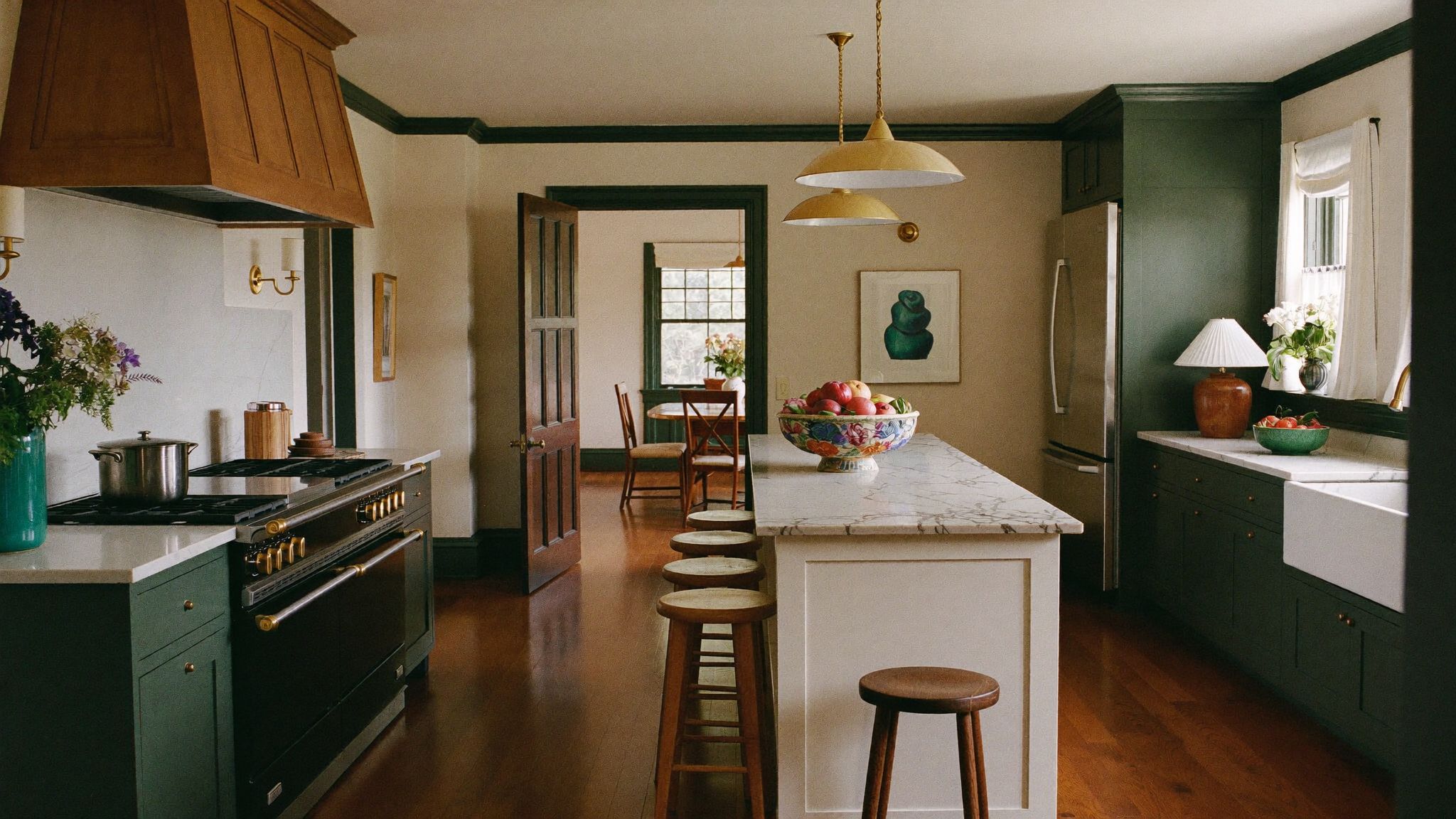 Deep view through a remodeled New England kitchen: soapstone-topped oak island, green cabinetry, paneled range hood, and the dining room beyond