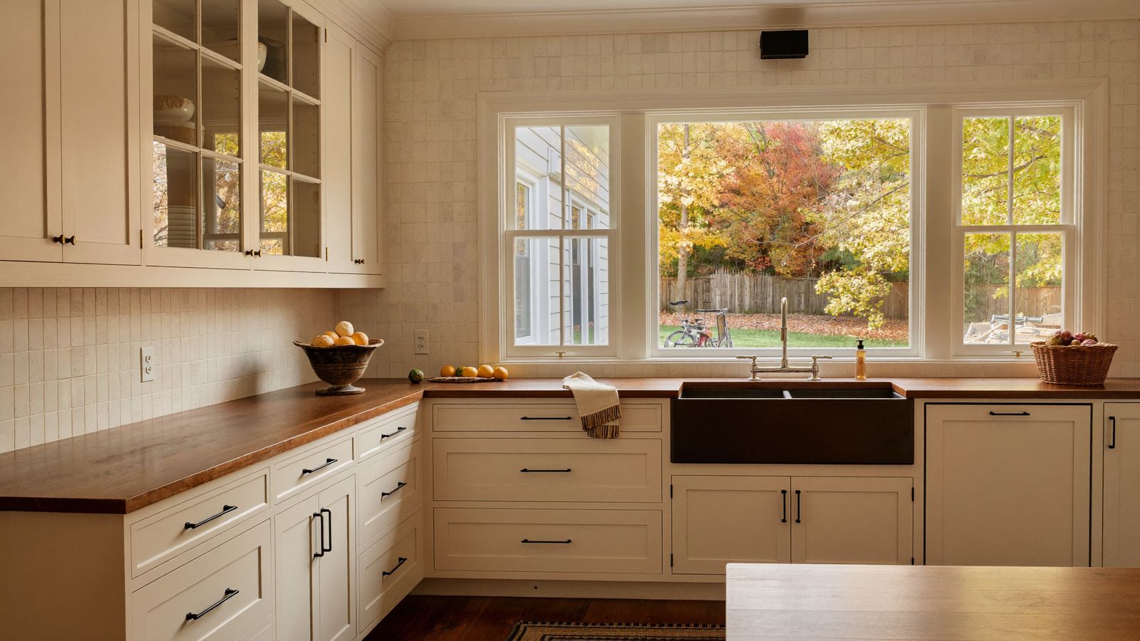 Renovated colonial kitchen with cream cabinetry, wood counters, and autumn foliage outside the window