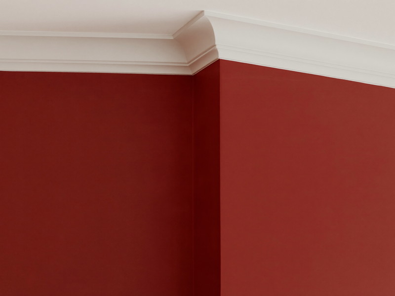 Close-up of a crisp hand-cut paint line where a deep oxblood wall meets bright white crown molding