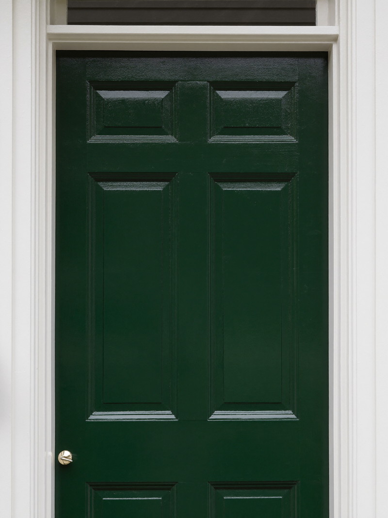 Front door freshly painted in deep forest green satin enamel with crisp bright white casing
