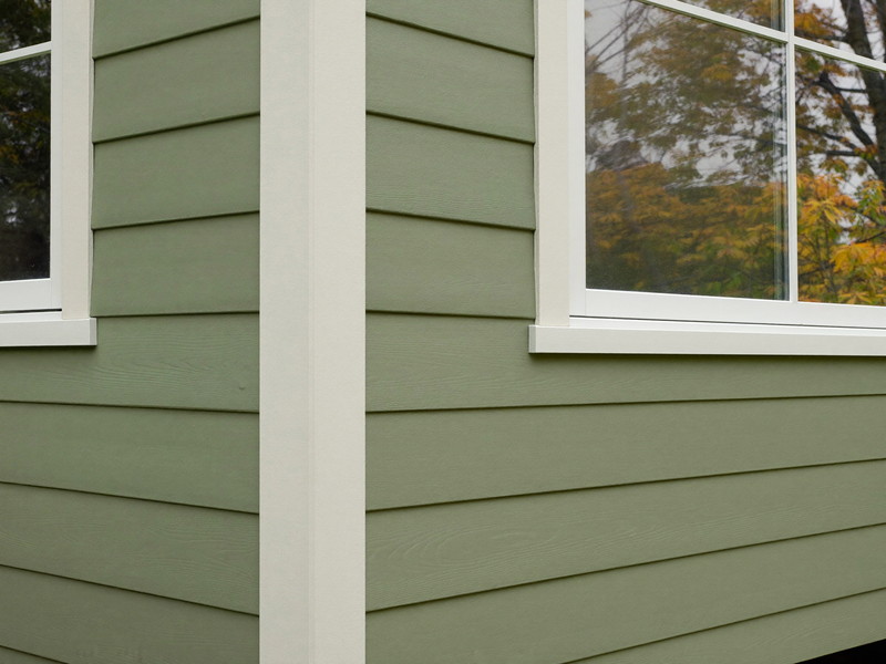 Sage green clapboard siding meeting a bright white corner board and window casing with sharp paint edges