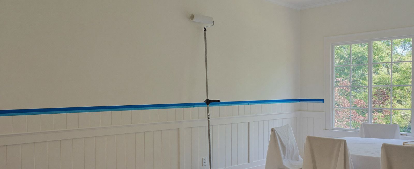 Dining room prepared for painting with taped wainscoting, drop cloths, and covered furniture