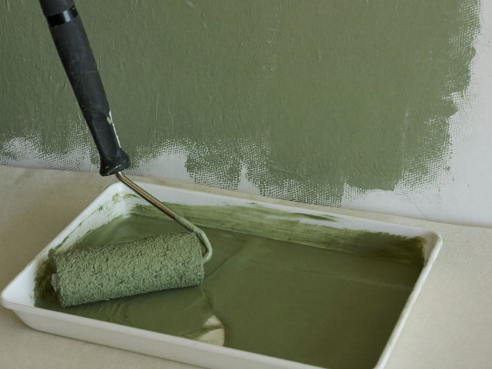 Paint roller resting in a tray beside a half-painted sage green wall