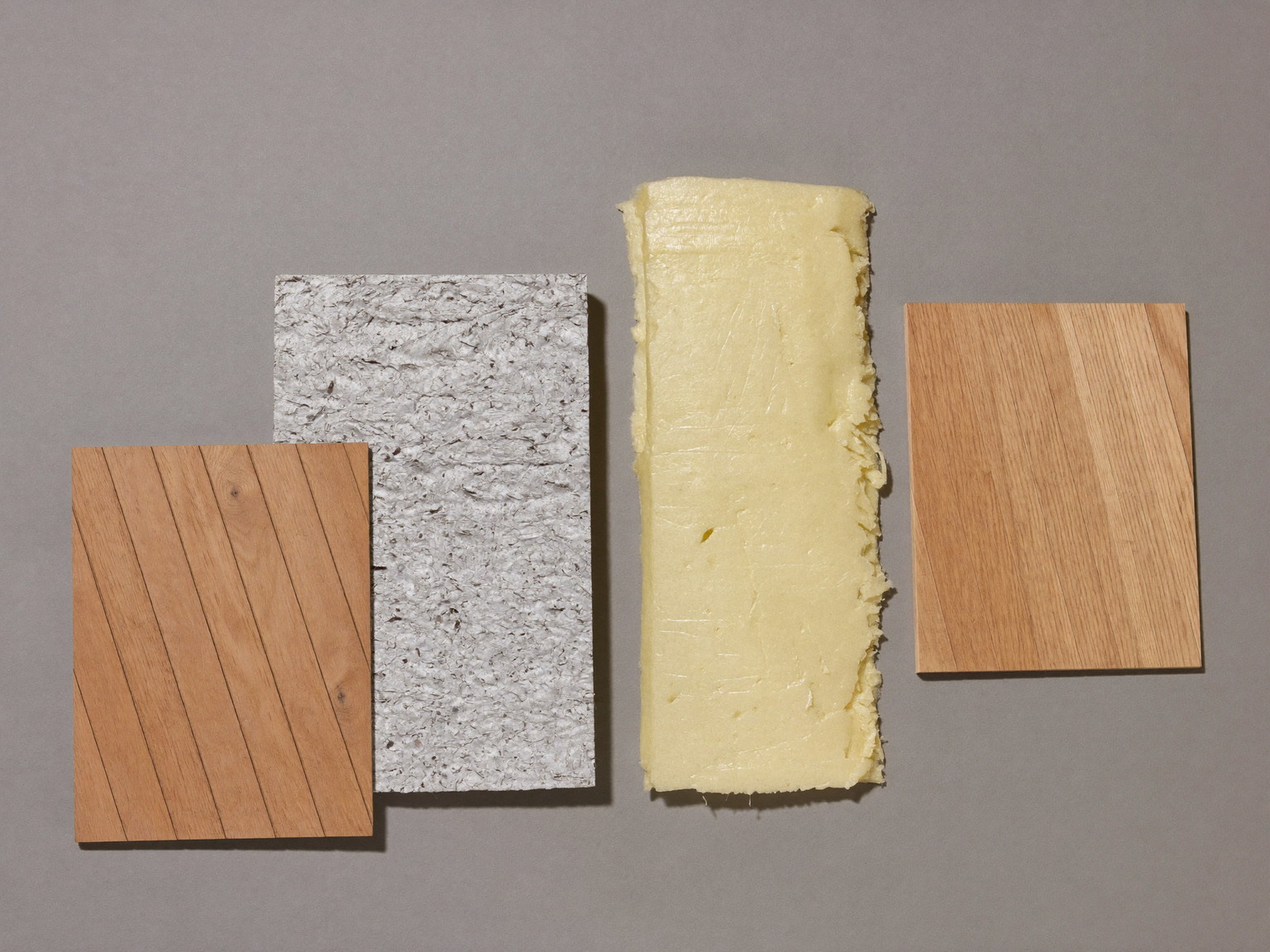 Moisture-smart basement materials arranged on a neutral grey surface: engineered oak plank samples, rigid foam insulation corner piece