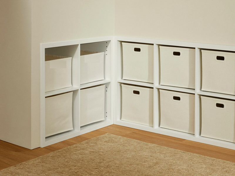 A bright finished lower-level playroom corner: warm white storage cubbies with plain unmarked canvas bins, soft oatmeal rug, engineered oak floor
