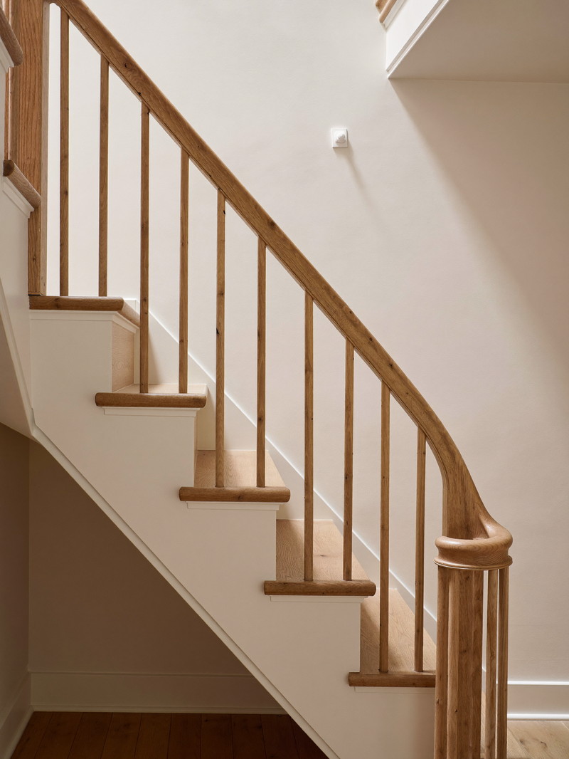 A renovated basement stair in an older home: warm oak treads with putty-painted risers and stringer, simple square balusters