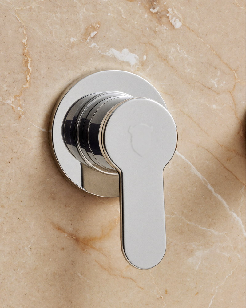 Macro detail of a polished chrome bath spout and smooth lever handle mounted on honed carrara marble, perfect machining, plain unmarked escutcheon