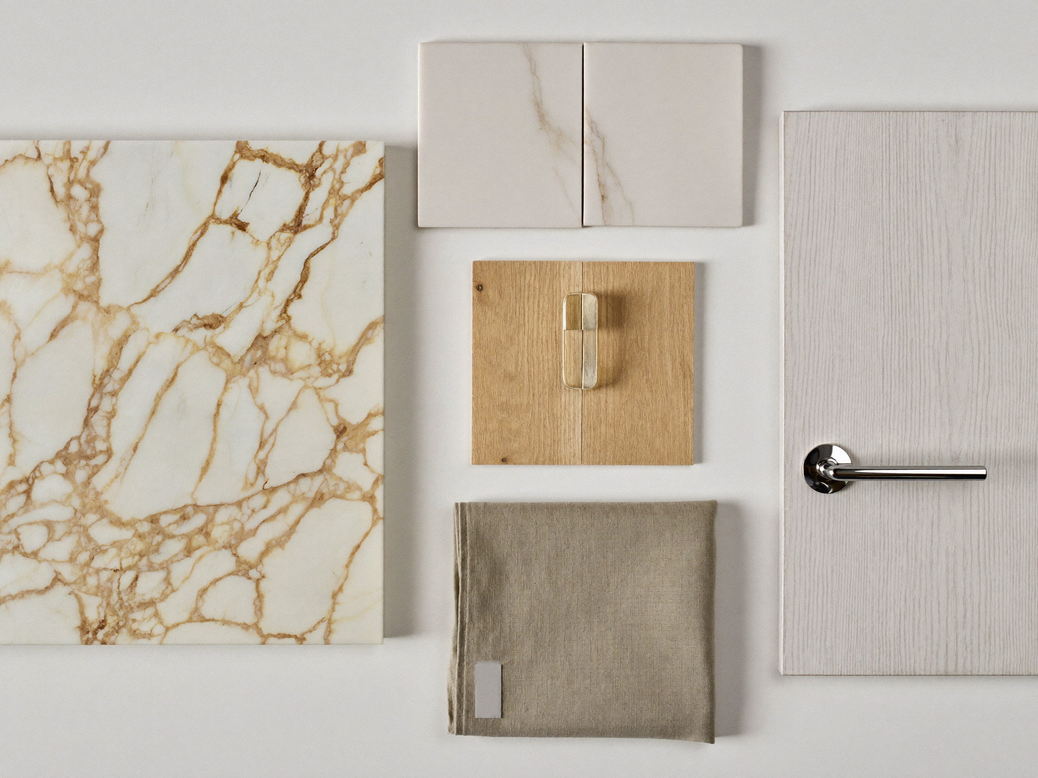 Bathroom material samples arranged on a warm white table: carrara marble square, white ceramic tile pair, white oak door sample