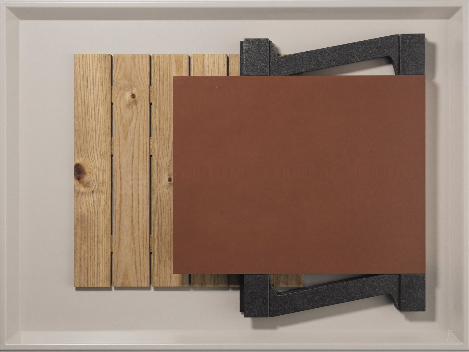 Decking materials on a neutral tray: cedar board sample, warm brown composite board sample, plain dark charcoal metal railing bracket with no markings