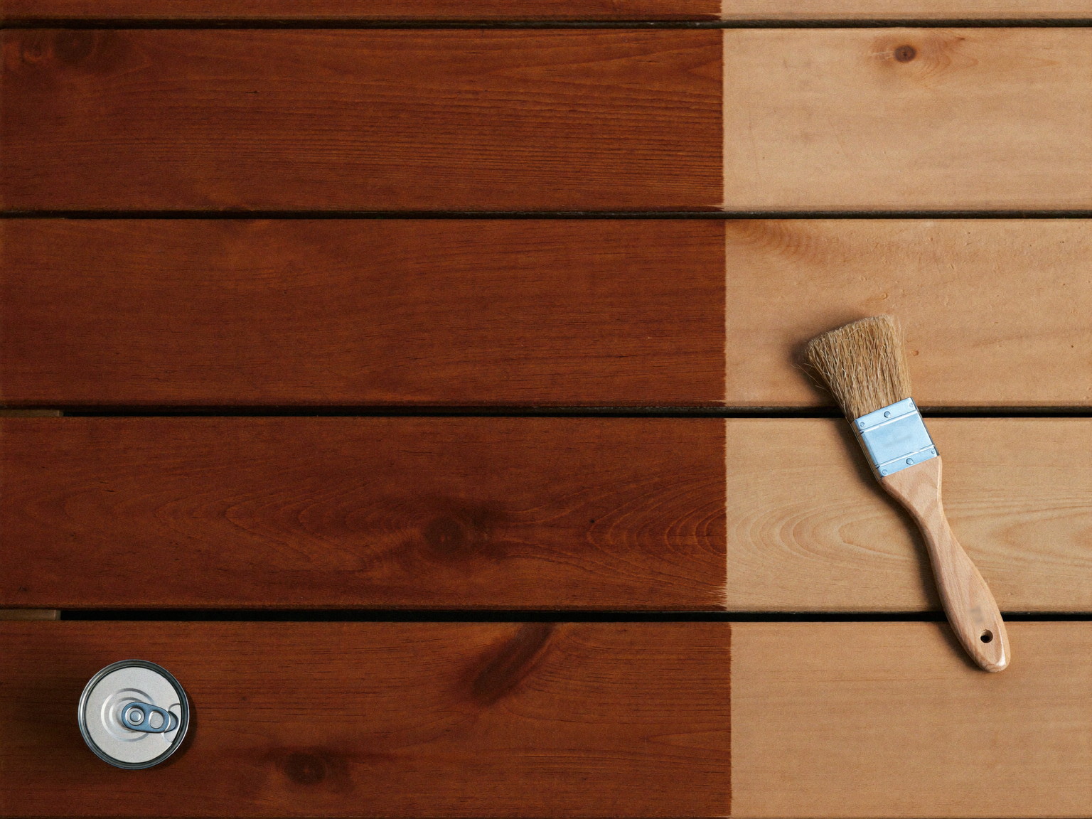 A small cedar deck mid-refinish seen from above: rich warm semi-transparent stain covering half the boards meeting bare sanded wood at a crisp brushed line