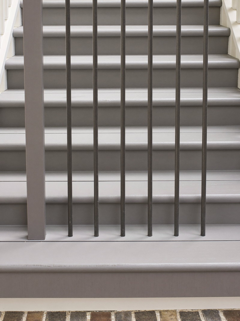 Exterior porch stairs on an older home: painted grey fir treads, white risers, slim dark charcoal metal balusters, brick walk below, crisp carpentry