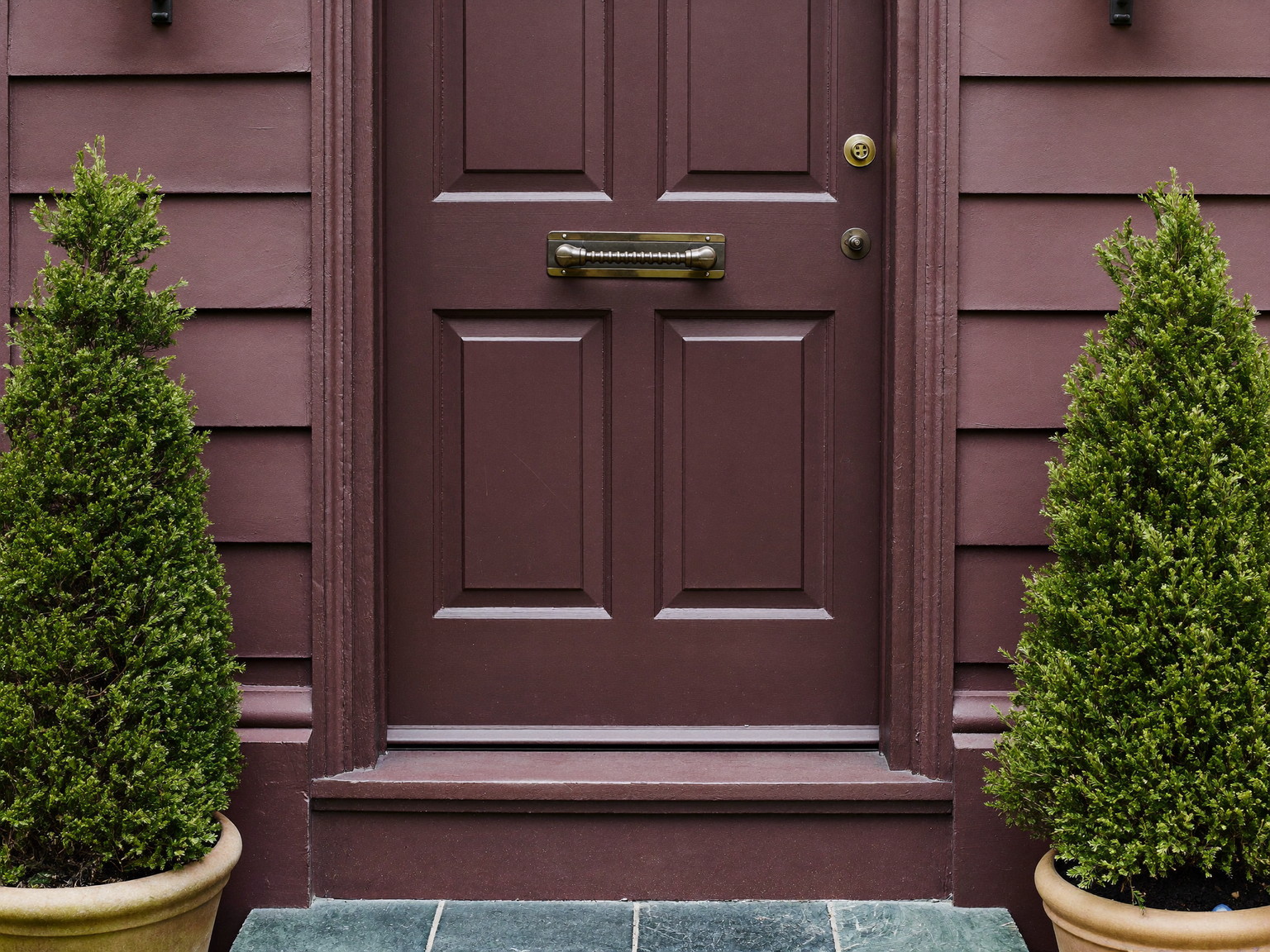 A cared-for older home entry: repainted paneled door in deep plum, repaired casing, polished plain oil-rubbed bronze hardware, swept slate step