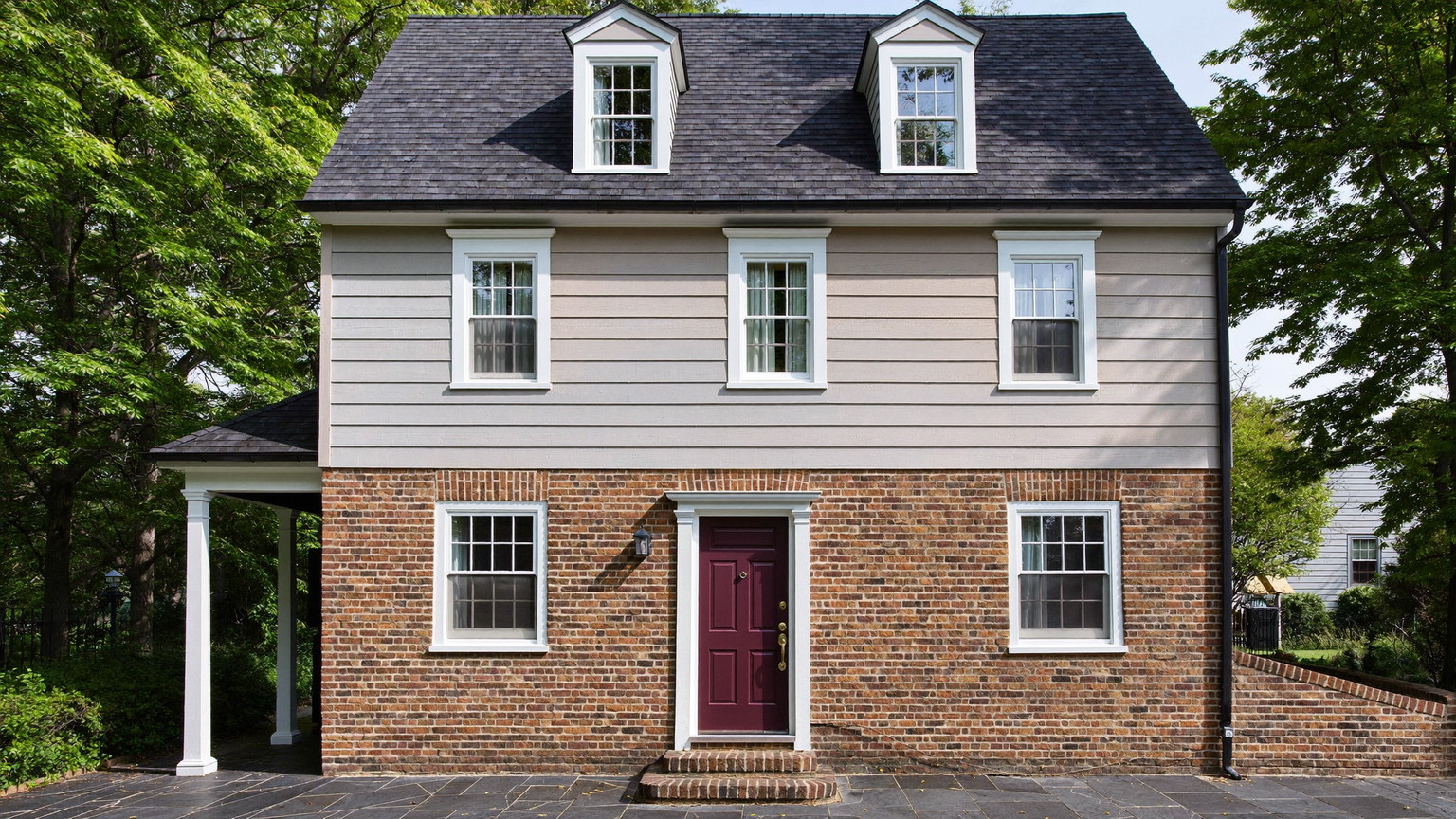 A beautifully kept older Brookline Massachusetts home facade: brick first story with warm clapboard above