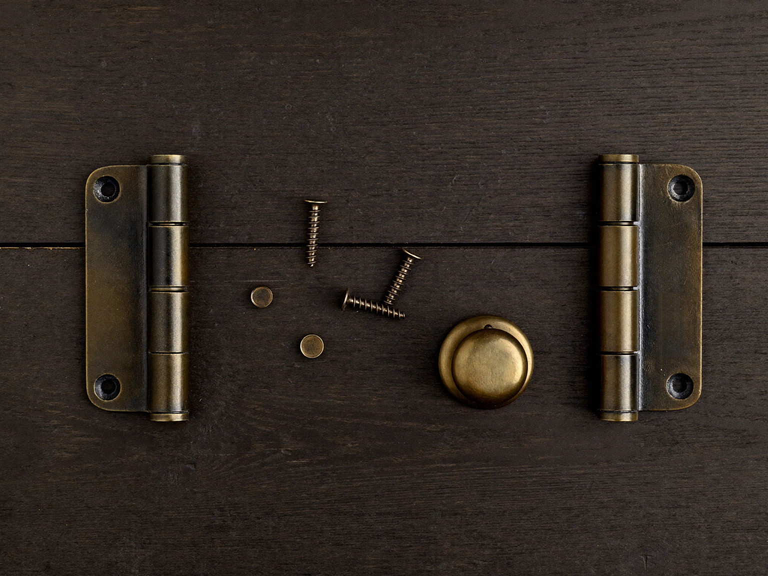 Quality door hardware laid out on dark stained oak: plain oil-rubbed bronze hinges, an unmarked knob, and smooth-headed screws with no stamps
