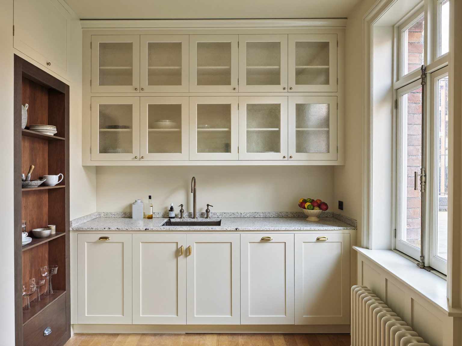 A completed compact urban kitchen: ivory inset cabinetry along one wall, walnut accents, pale granite counters, aged nickel fixtures