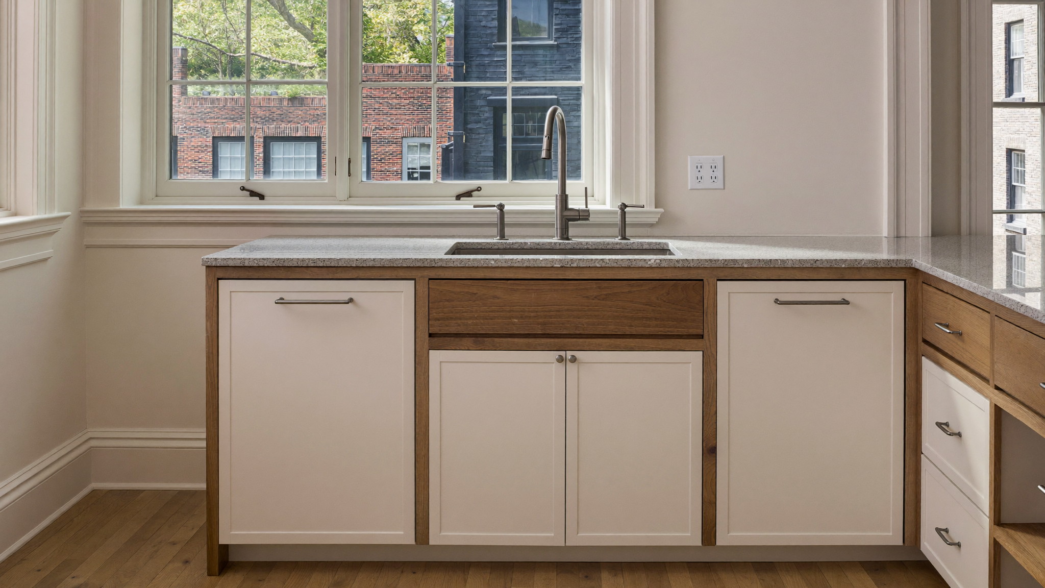 Editorial photograph of a renovated compact kitchen in an older Brookline Massachusetts home: ivory inset cabinetry with walnut open frame accents