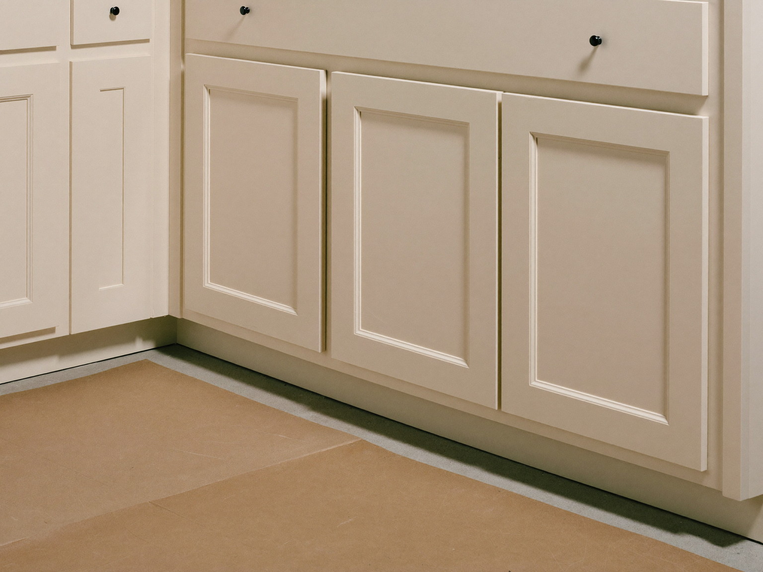 A kitchen renovation mid-install in an older home: ivory inset cabinets installed and shimmed level, unmarked cabinet doors leaning nearby