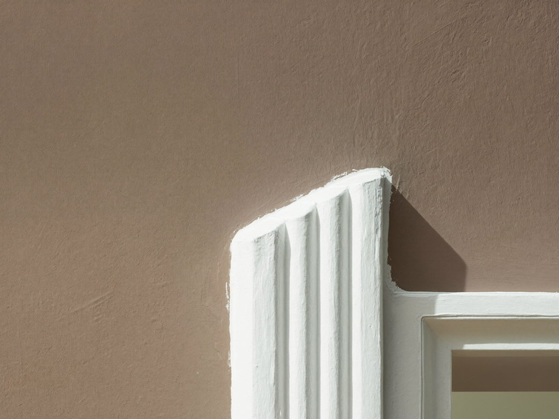 Close-up of a crisp hand-cut paint line where a warm mushroom-taupe wall meets bright white painted period trim, razor-straight edge, raking light