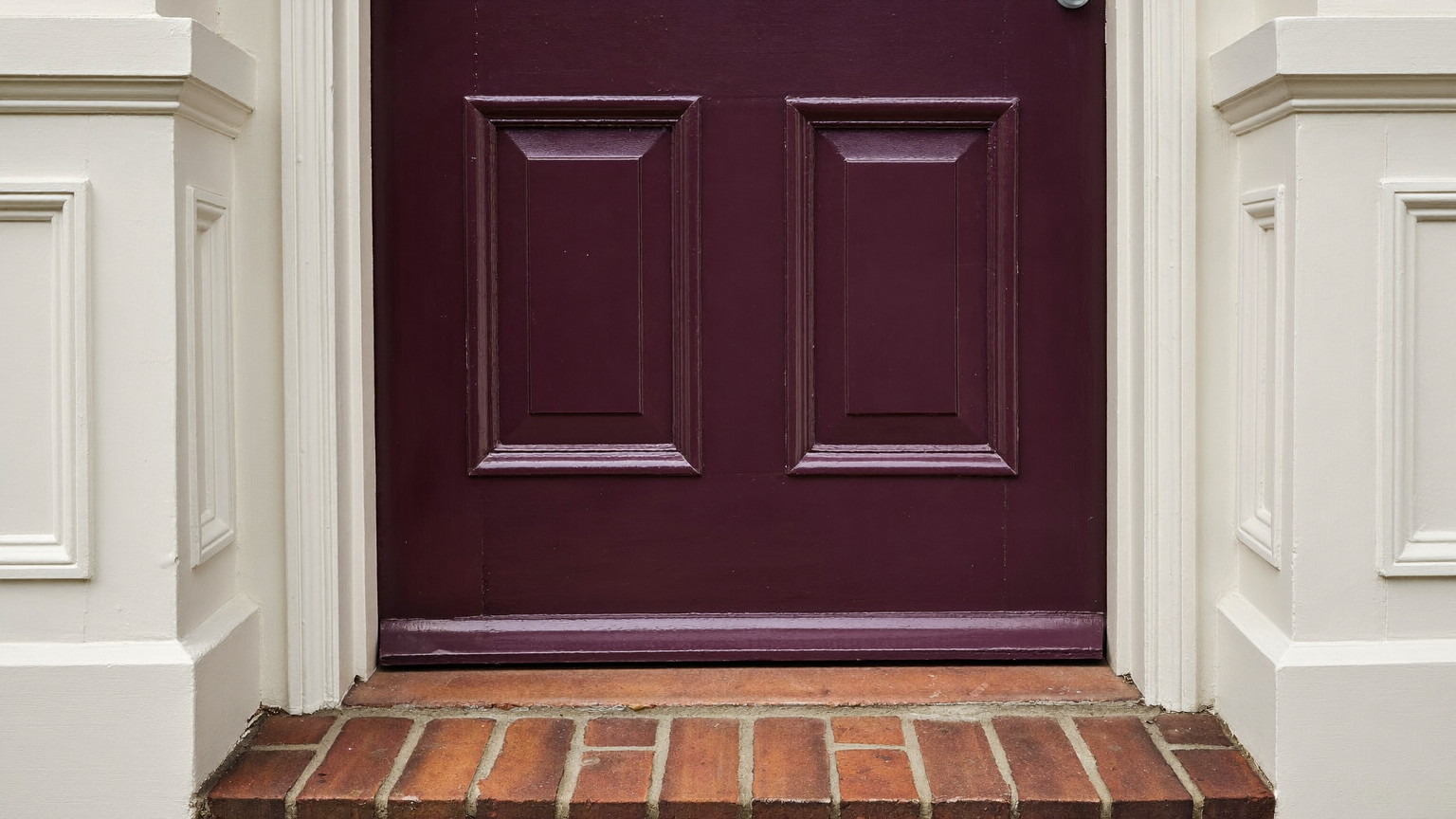 A freshly painted entry of an older Brookline Massachusetts home: deep plum-aubergine front door in satin enamel with crisp edges