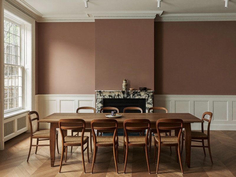 An older-home dining room with warm mushroom-taupe walls above crisp white panel wainscot, marble fireplace surround