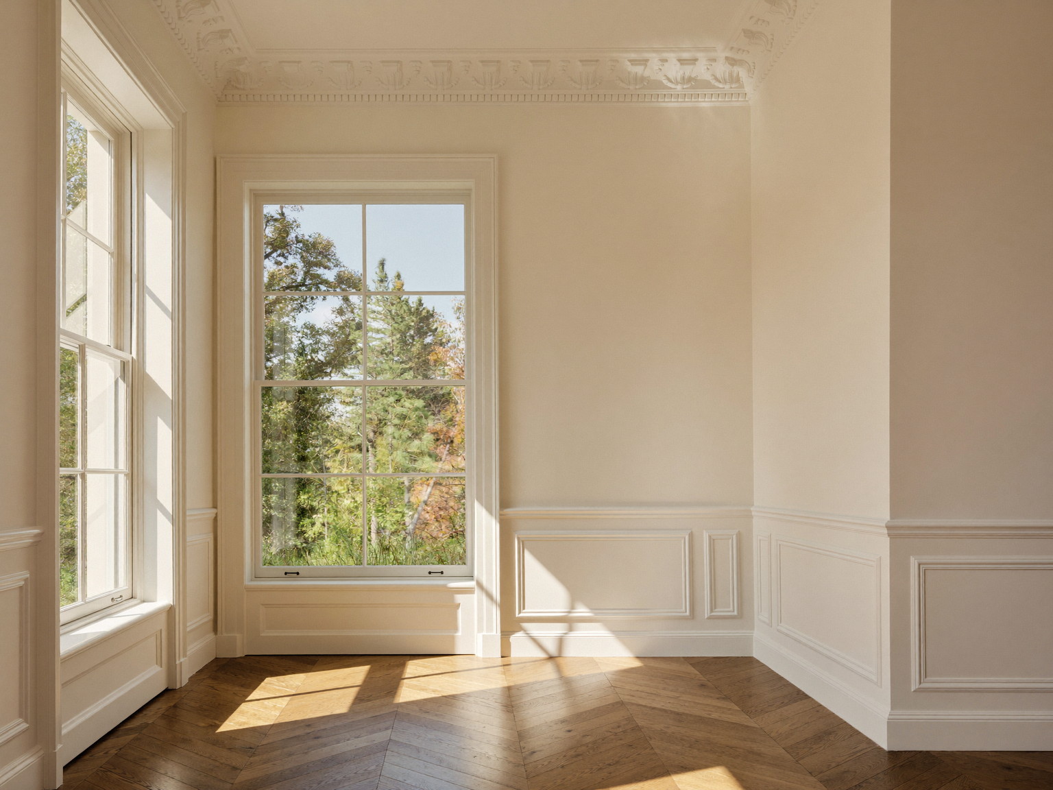 A finished parlor with fresh warm white walls, ornate crown molding crisply painted, tall windows with deep casings