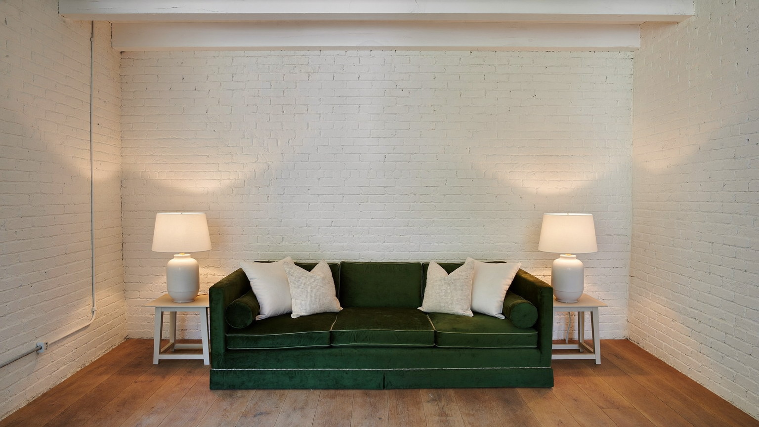 Editorial photograph of a finished lower-level family snug beneath an older Cambridge Massachusetts home: warm white painted brick foundation walls, deep green