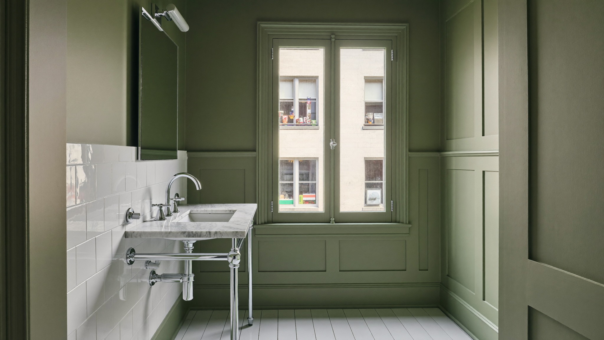 Editorial photograph of a renovated compact bathroom in an older Cambridge Massachusetts triple-decker condo: sage-green painted wall paneling, white