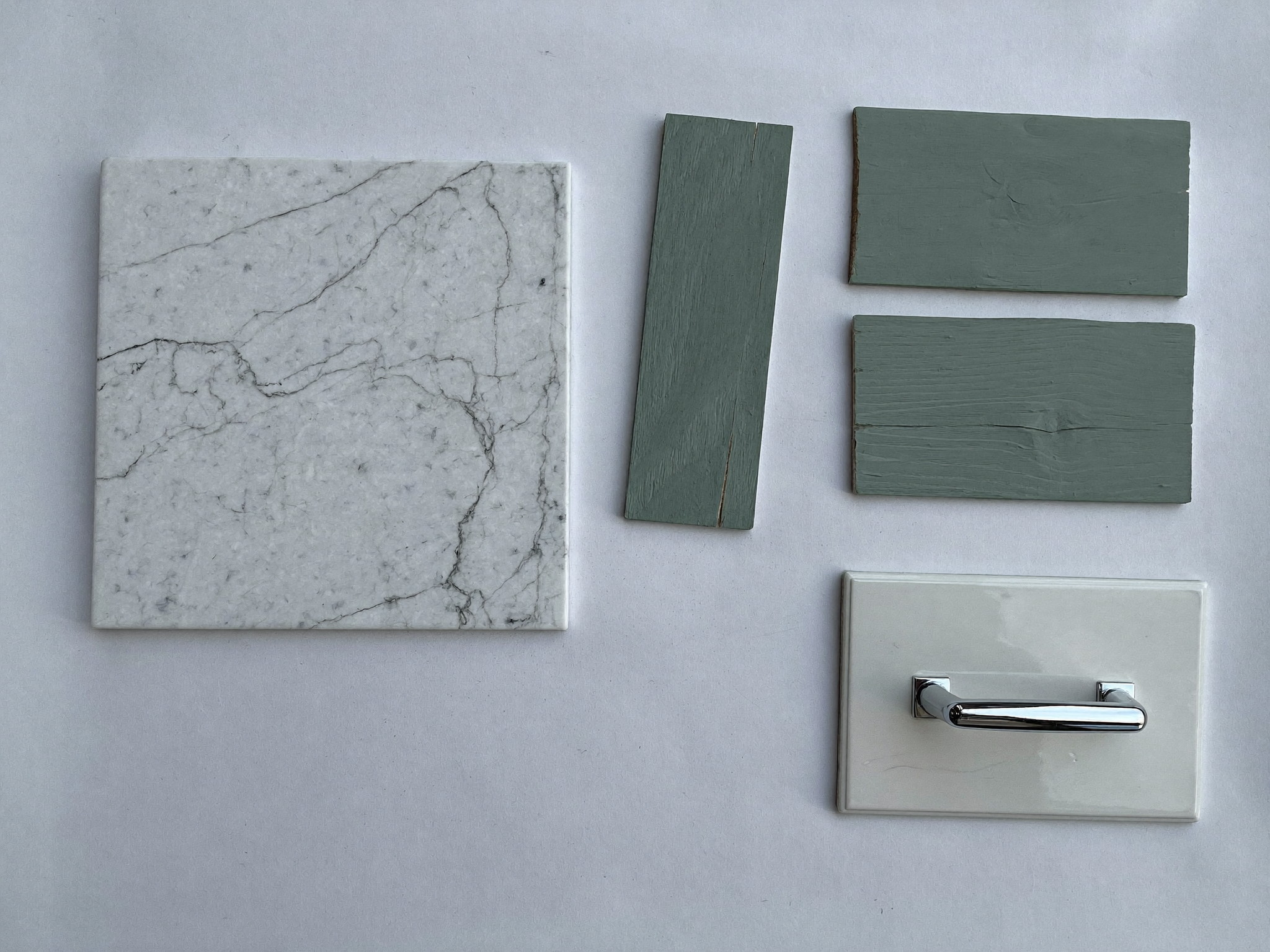 Overhead flat-lay on plain white paper: one square slab sample of white carrara marble with soft gray veining, three loose rectangles of sage-green painted